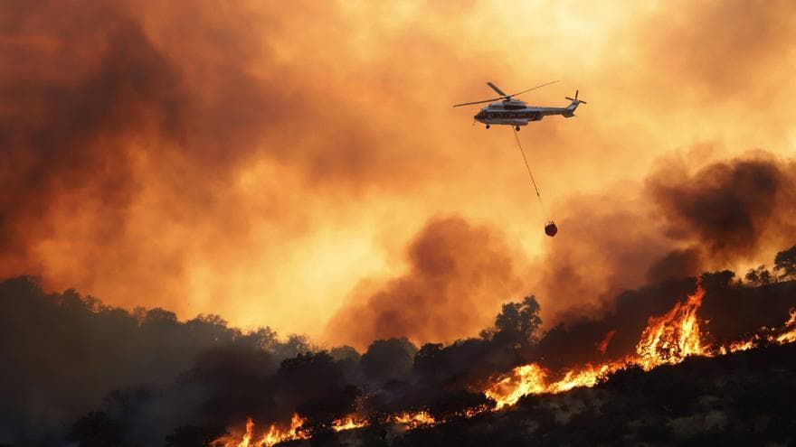 Helicóptero antiincendios trabajando sobre un frente de fuego en una ladera de monte mediterráneo.